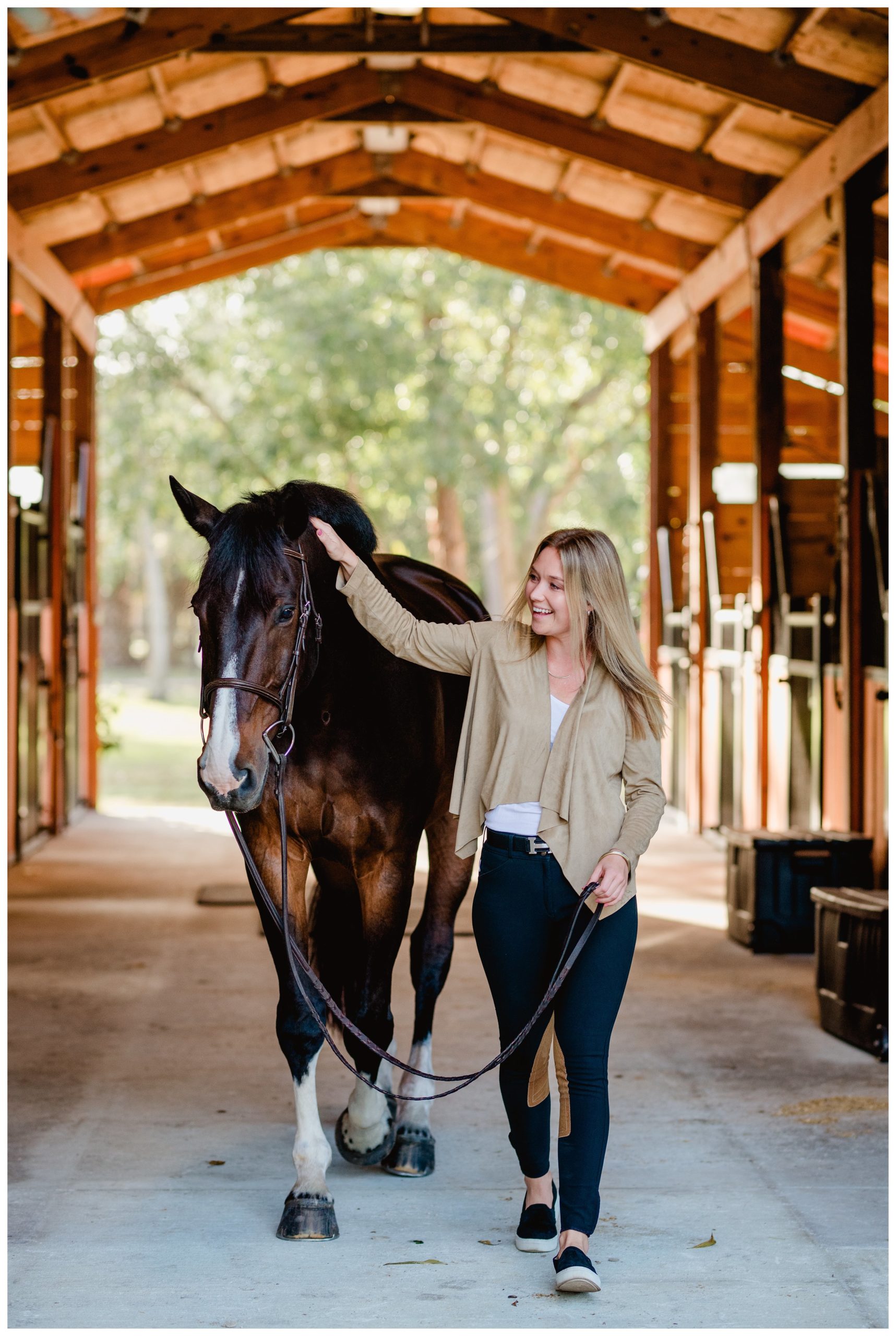 Equestrian photographer in Florida takes photos of horse and owner walking down barn aisle.