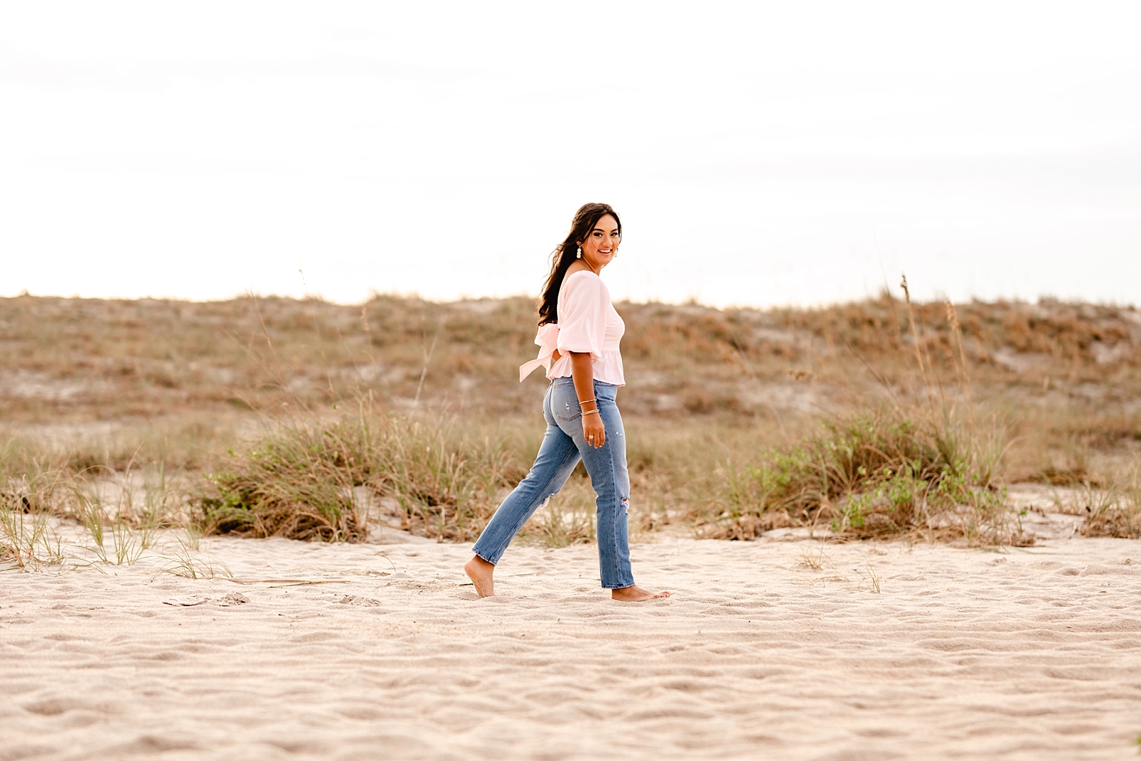 Girl in pink shirt and jeans on Florida beach at sunset. North Florida high school senior photographer. Painted Oak Photography.