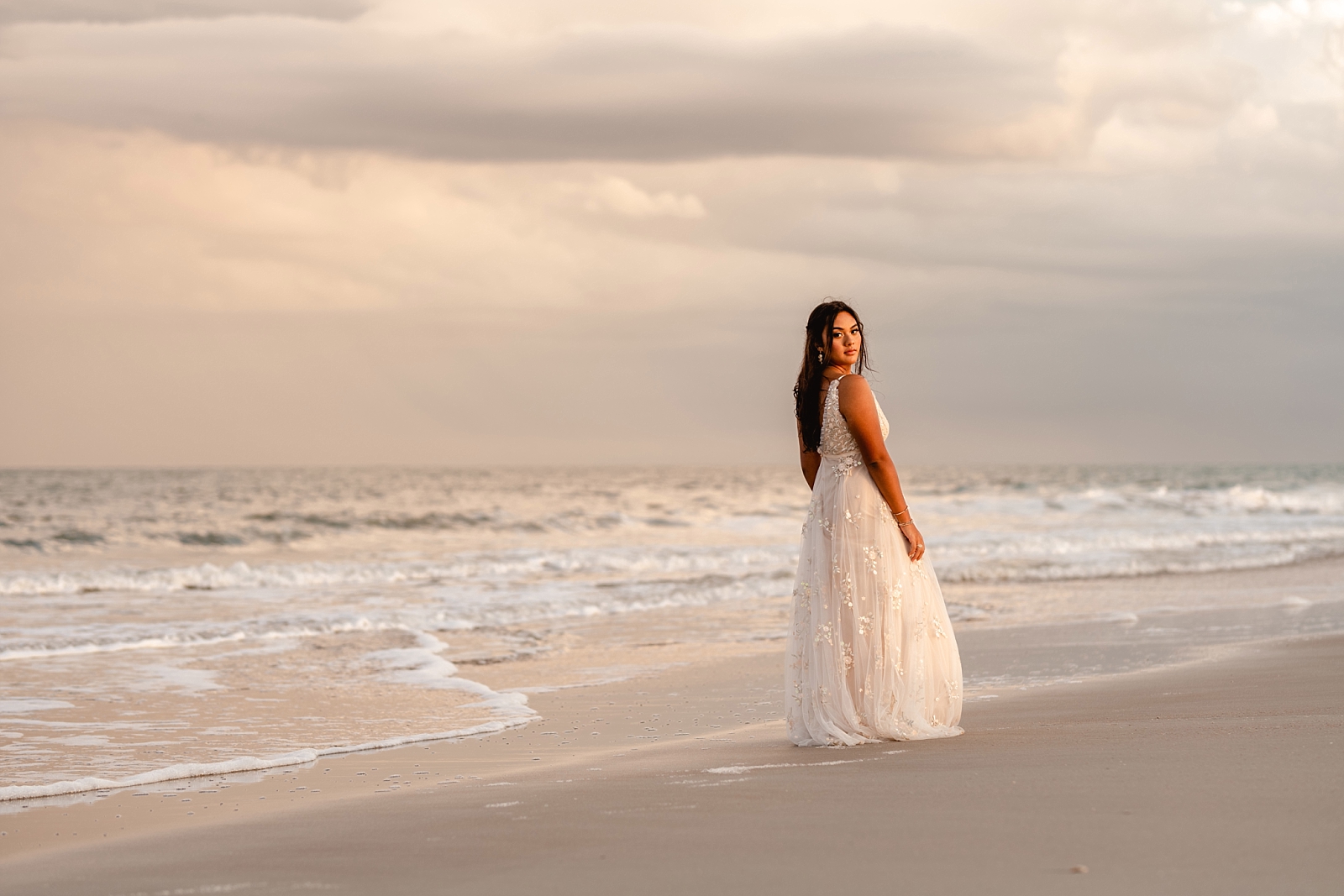 Sunset pictures on the beach for senior girl in a long, flowy, white dress with moody storm clouds in the background. Senior Photographer, Painted Oak Photography.