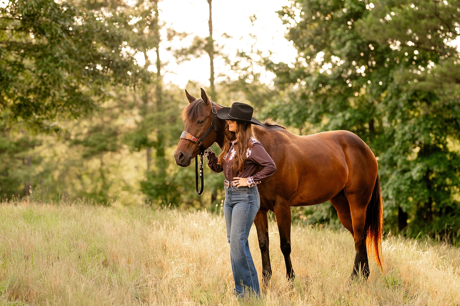 Barrel racer poses with her horse wearing cowgirl hat and cow hide shirt.