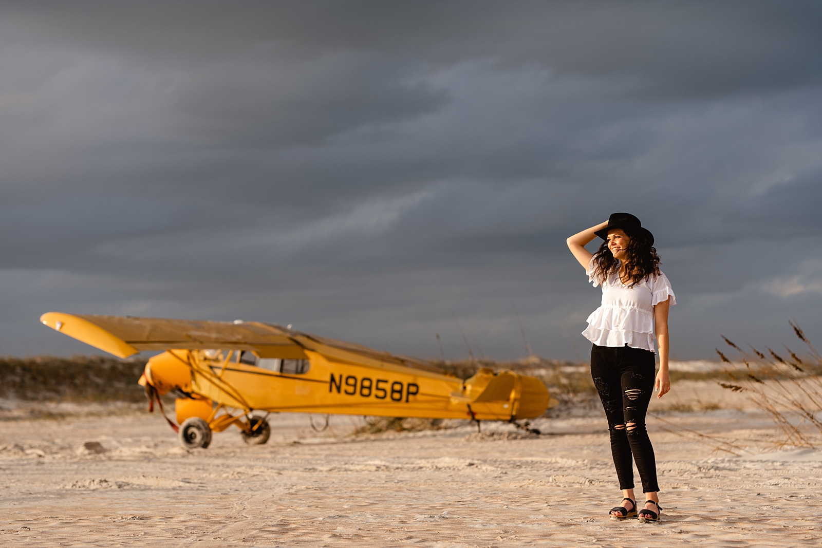 Senior photos on the beach in Florida with airplane and stormclouds in the background.
