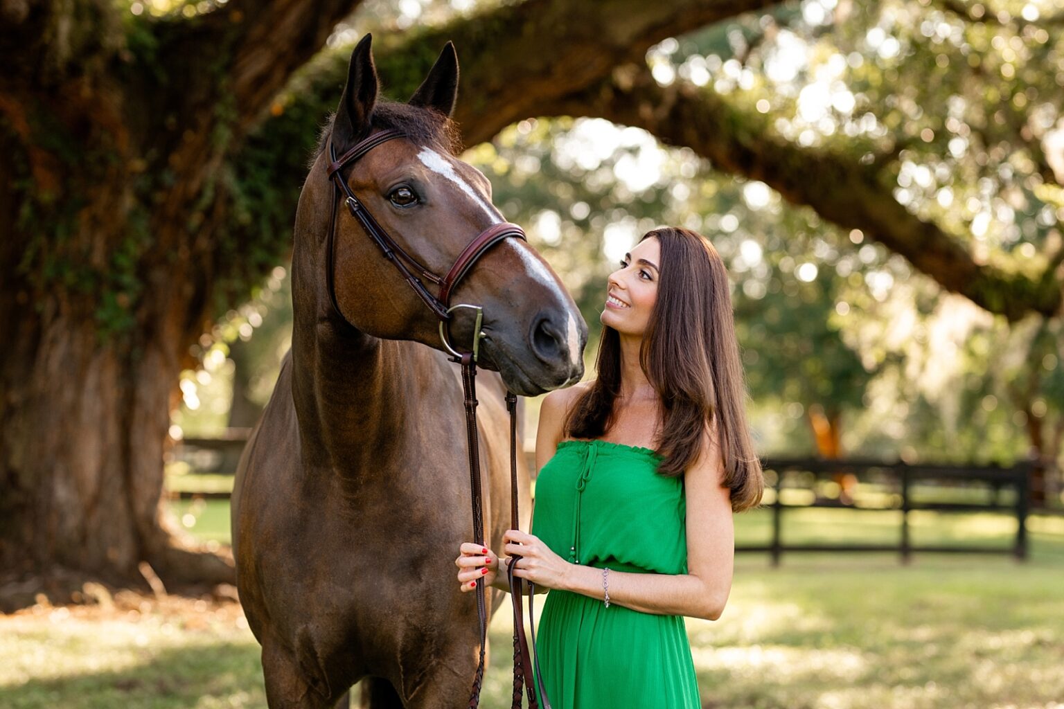Best horse photographer in Tallahassee takes photos of woman in gorgeous green dress with her Warmblood horse underneath historic oak trees. Posing ideas for horse and rider photoshoot.