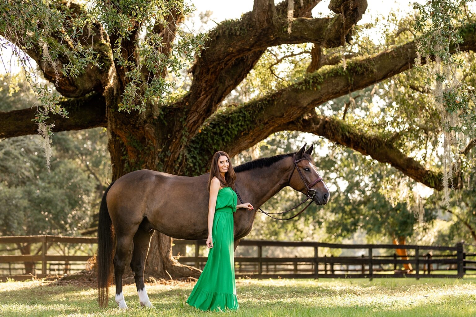Best horse photographer in Tallahassee takes photos of woman in gorgeous green dress with her Warmblood horse underneath historic oak trees. Posing ideas for horse and rider photoshoot.