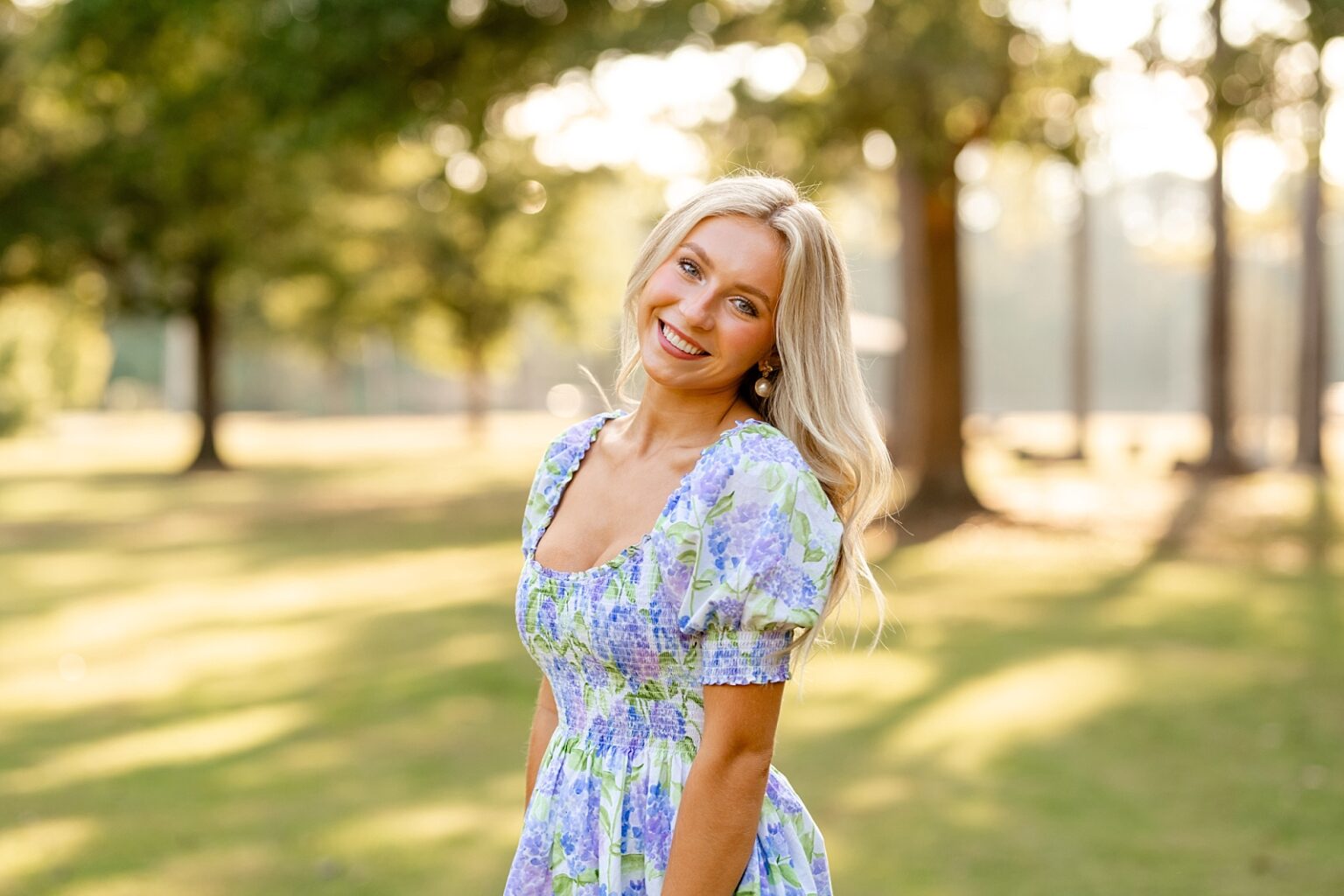 Girl takes senior pictures in pretty purple floral dress. Outfit ideas for senior pictures. Senior photos in Birmingham, senior portraits, creek photoshoot, sunset photography, high school senior photographer
