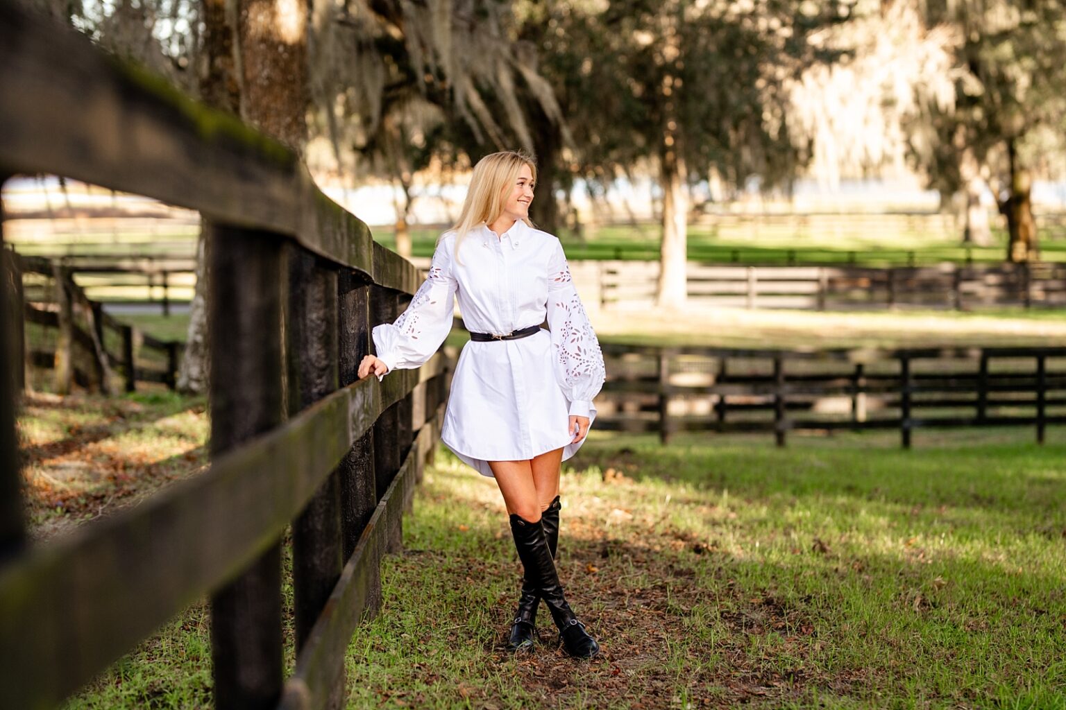 Equestrian inspired senior outfit for senior pictures. White dress with equestrian belt and tall boots. Ocala, FL. Hunter/jumper rider.