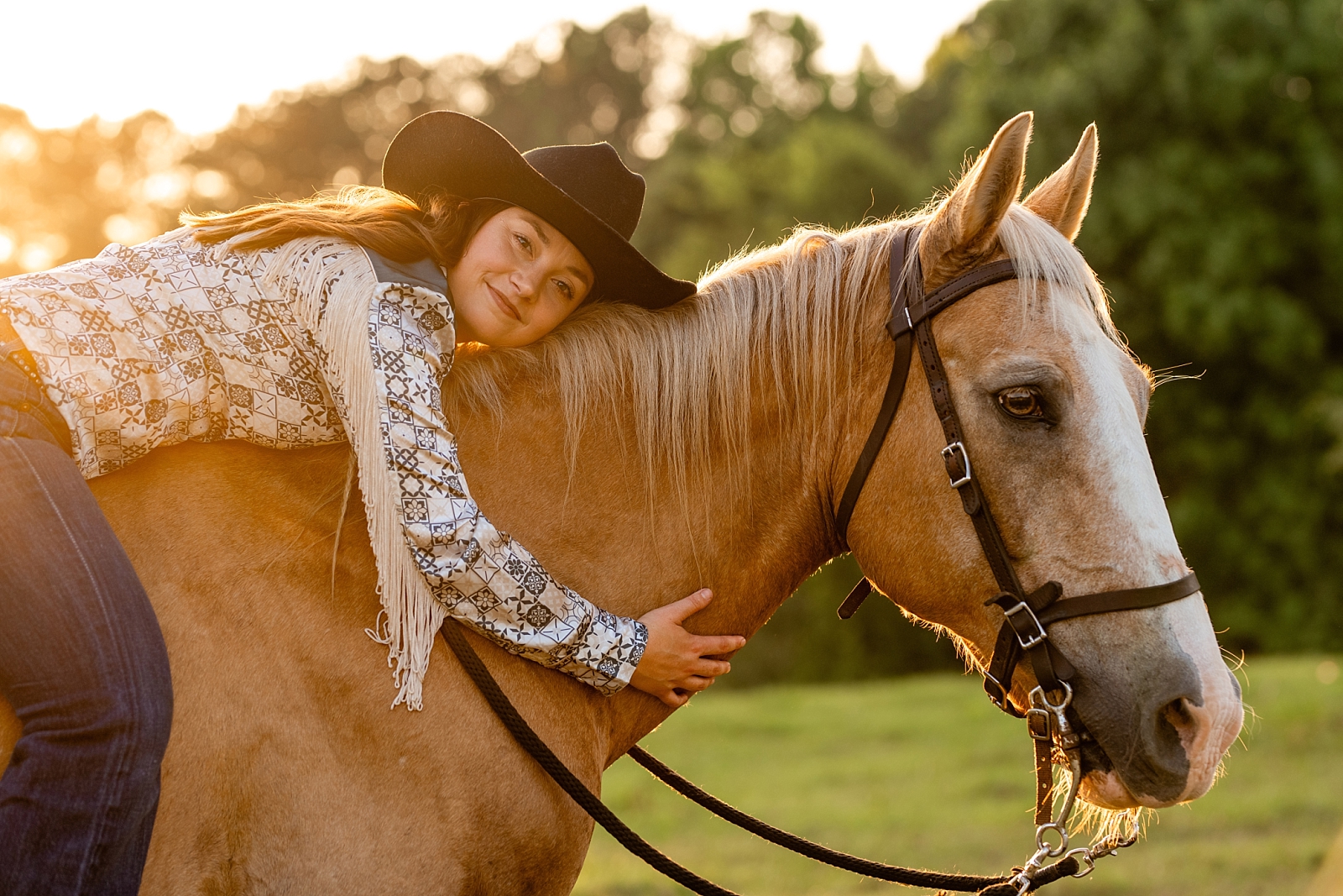 Equestrian photographer in Alabama takes photos of woman with her older horse at golden hour sunset. Palomino. Fringe. Western Outfit. Western style. Cowgirl.